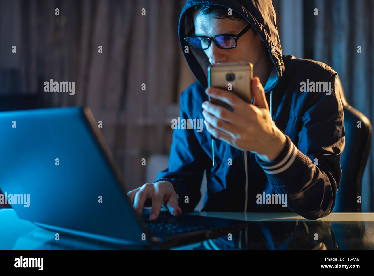 Hacker in the hood holding the phone in his hands trying to steal access databases with passwords. The concept of cyber security Stock Photo