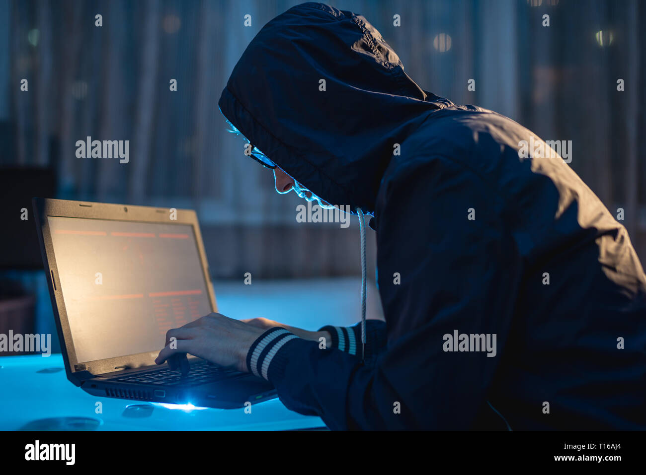 Cybercriminal hacker in the hood typing program code while stealing access databases with passwords. Hackers and cyber security concept Stock Photo