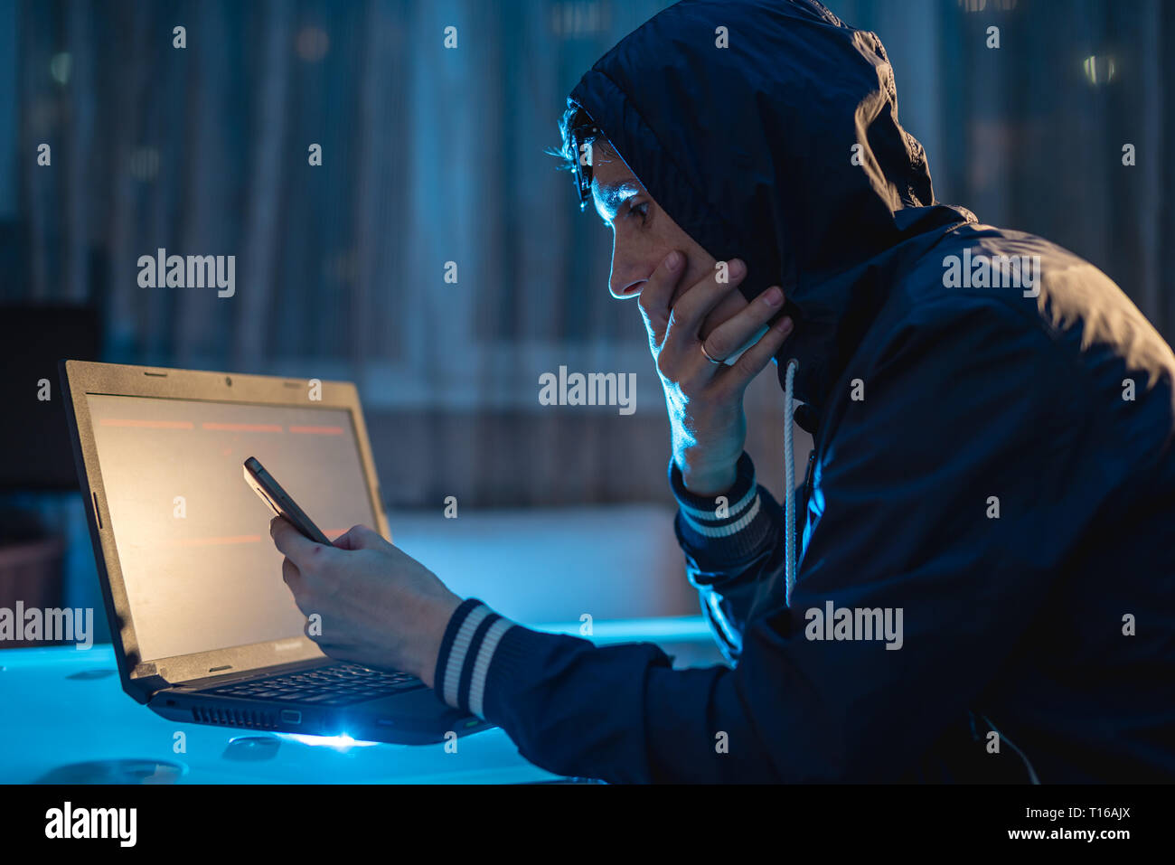 Cybercriminal hacker in the hood typing program code while stealing access databases with passwords. Hackers and cyber security concept Stock Photo