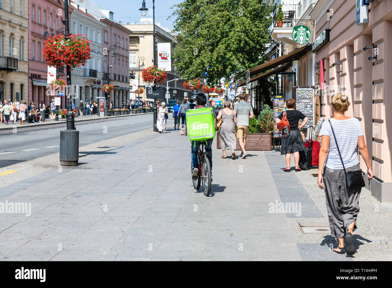 Warsaw, Poland - August 23, 2018: Uber eats bicycle man with green bag in old town historic street in capital city during sunny summer day called Krak Stock Photo