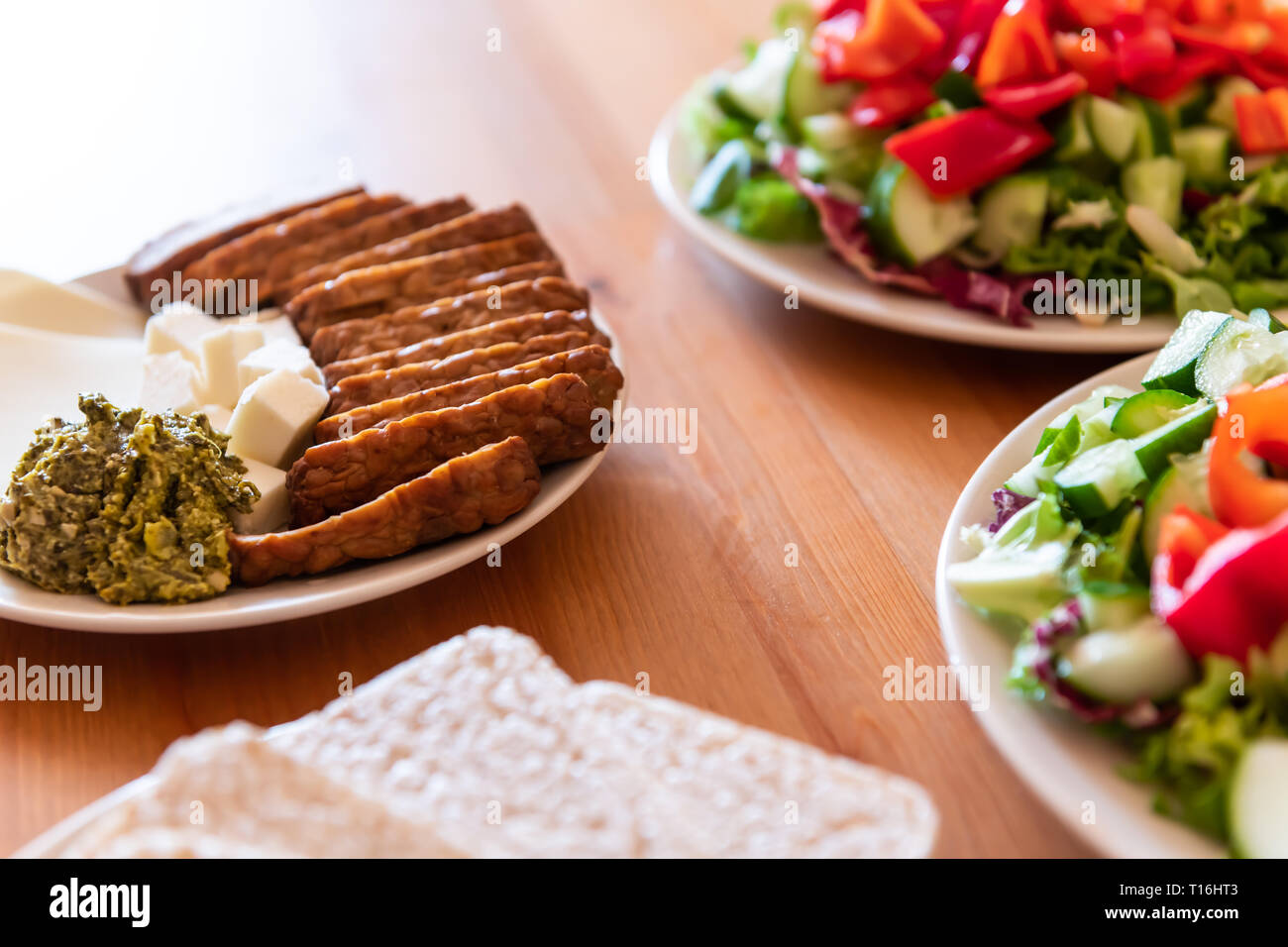 Healthy vegan vegetarian lunch or dinner green vegetables salad with table setting and tempeh slices with pesto and rice cakes Stock Photo