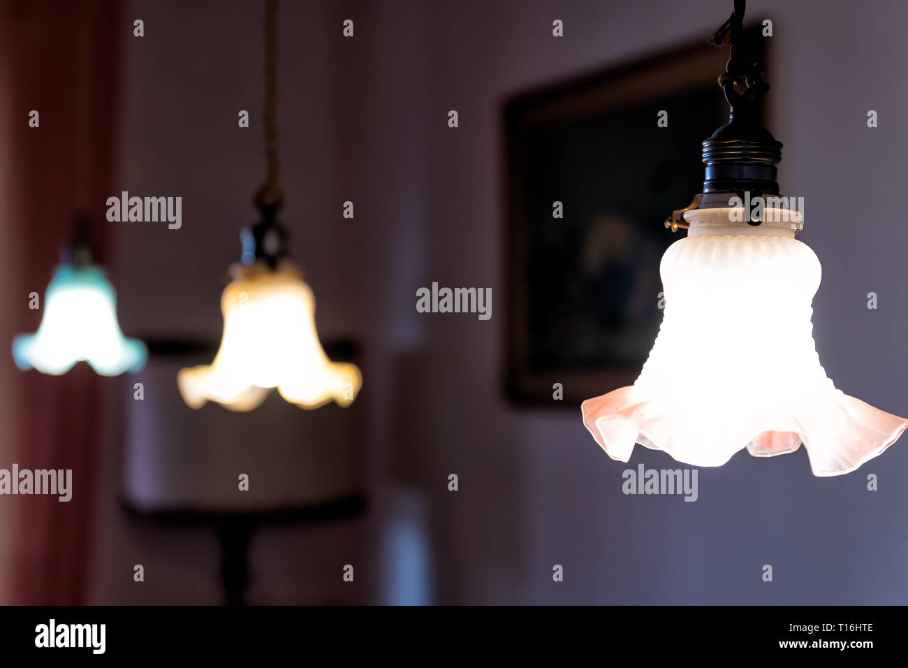 Closeup of three hanging ceiling lamps in home with dark room and illuminated yellow green fixtures in row Stock Photo