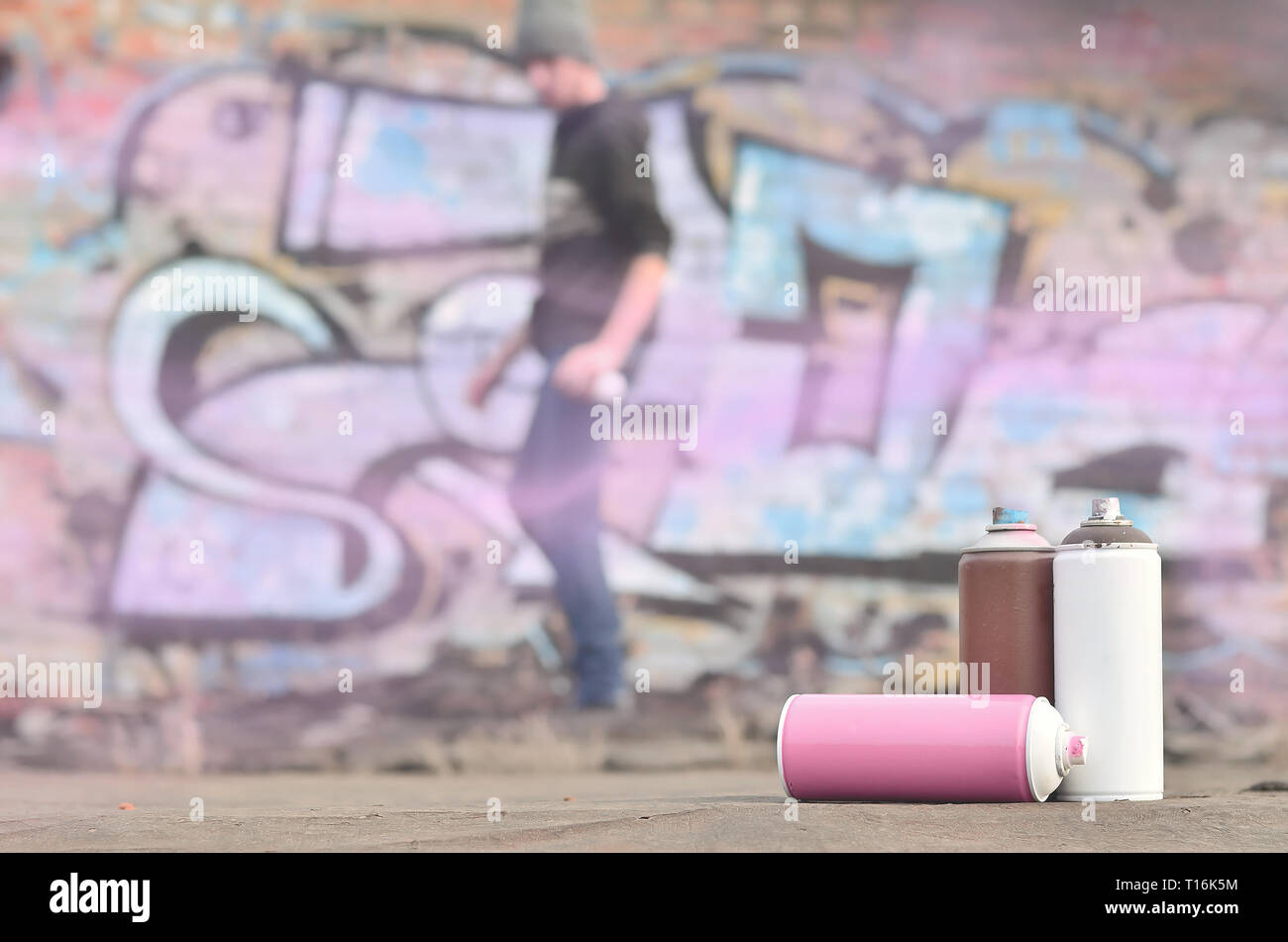 A photography of a certain number of paint cans against the background of the space with the wall on which the young guy draws a large graffiti drawin Stock Photo