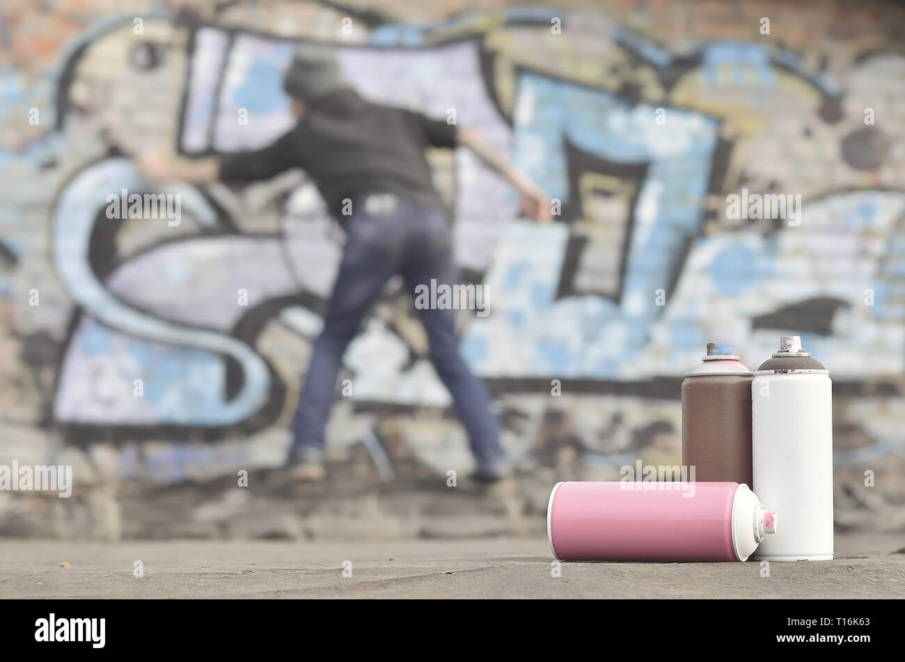 A photography of a certain number of paint cans against the background of the space with the wall on which the young guy draws a large graffiti drawin Stock Photo