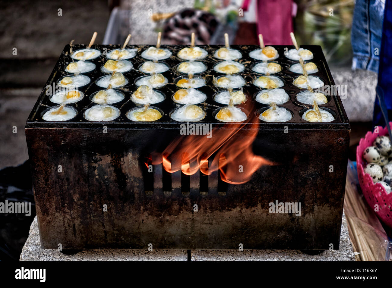 Thailand street food with quail eggs cooking on a flame stove at a Thai market stall. Stock Photo