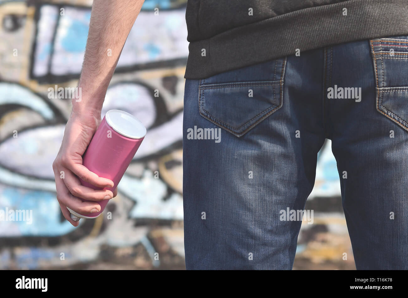 A photo of a bully who spoils state property, paints walls with aerosol paint. Fragment of the body of a young criminal vandal with a paint sprayer in Stock Photo