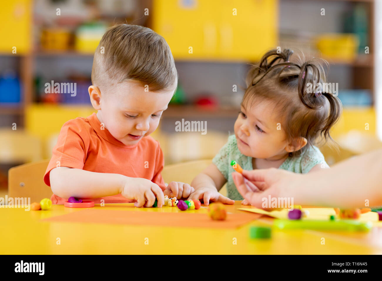 Kids boy and girl play in kindergarten with interest. Children sculpt from plasticine in day care centre. Stock Photo