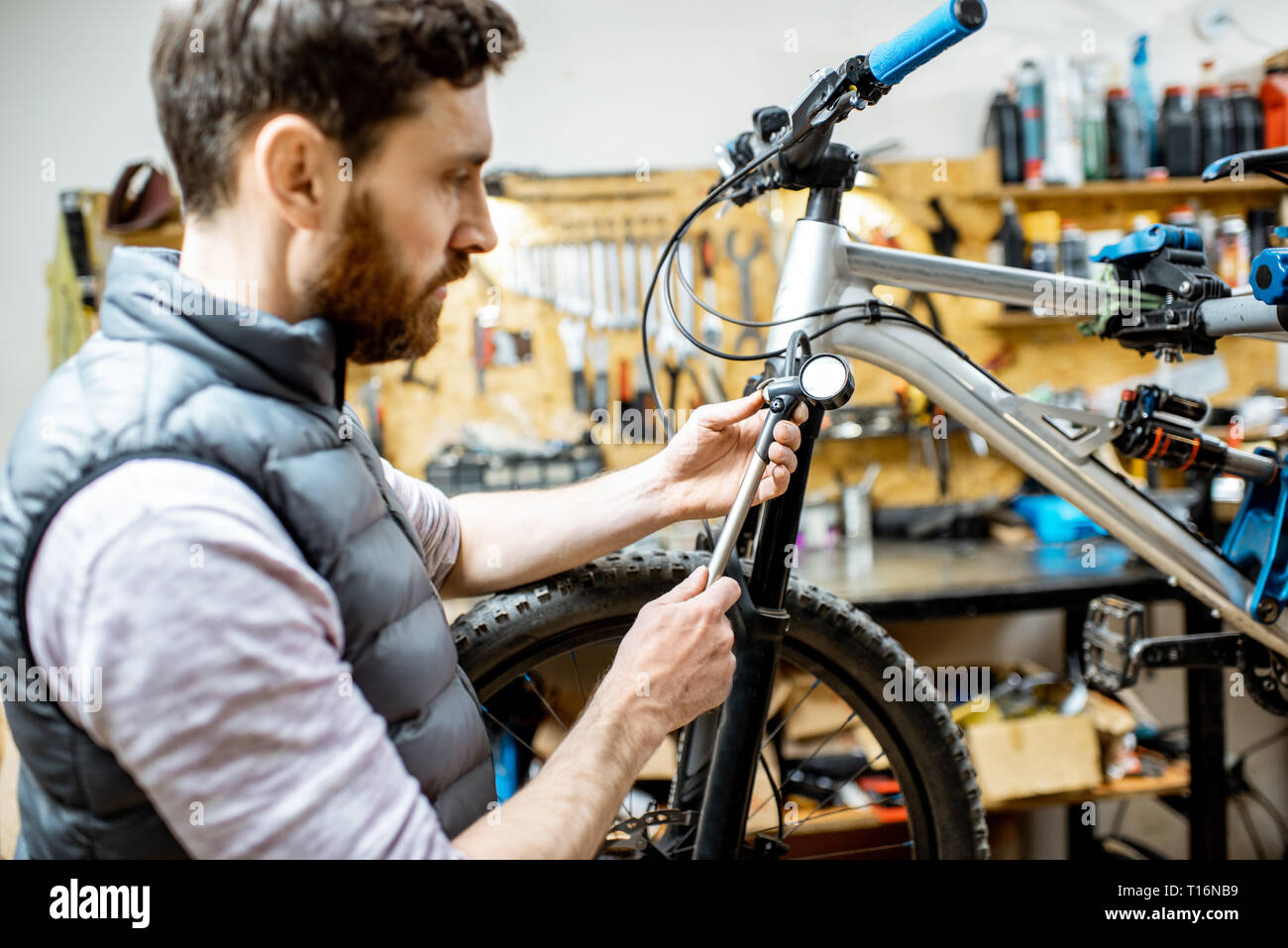 Repairman serving a bicycle, checking a air pressure in the pneumatic absorber of a fork in the workshop Stock Photo