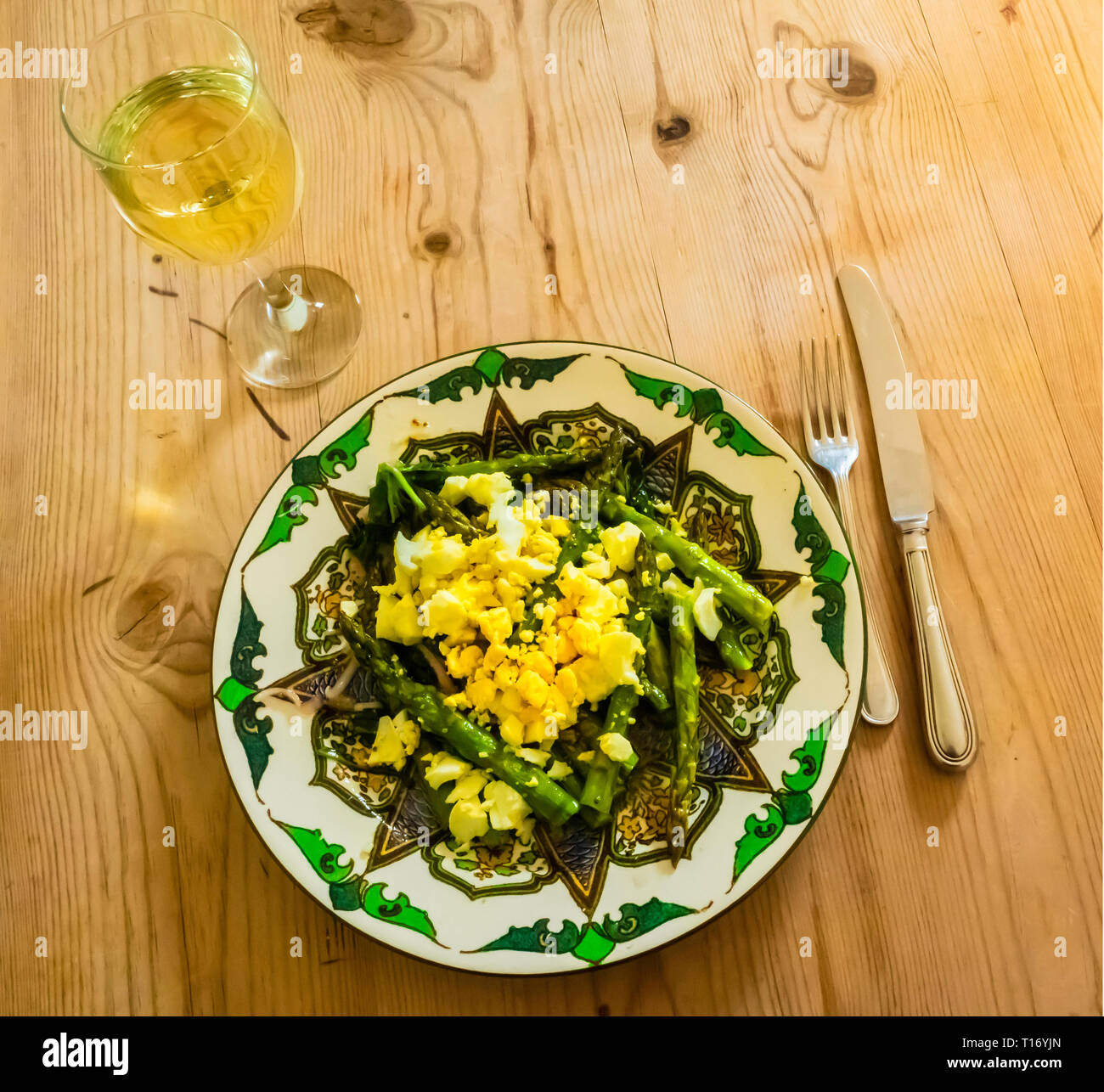 A light lunch of Asparagus Mimosa made with chopped hard-boiled egg and shallots served on a fancy plate on a wooden table Stock Photo