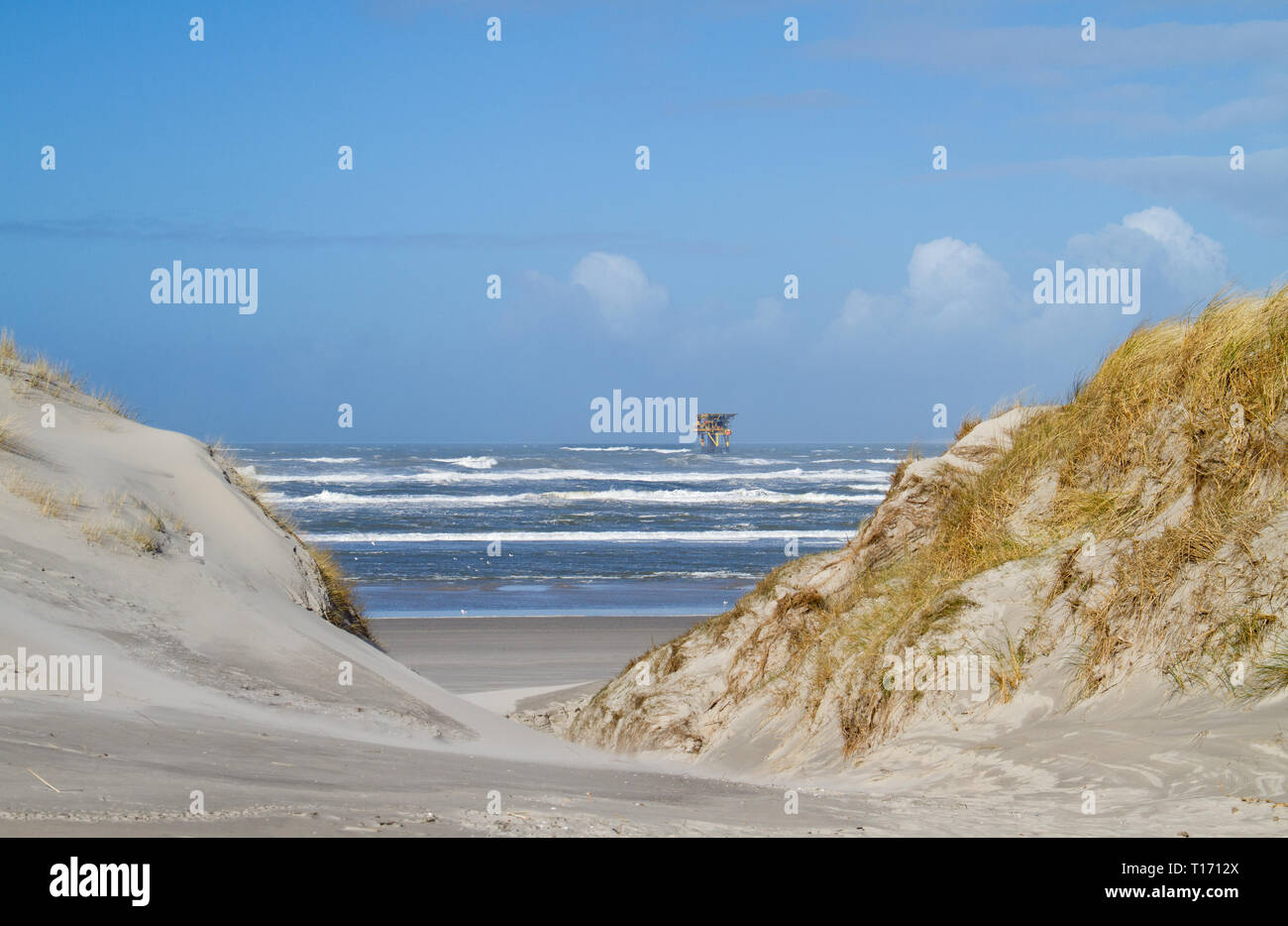 Offshore production platform near the Dutch island Ameland, dunes, beach and breaking waves in the foreground Stock Photo