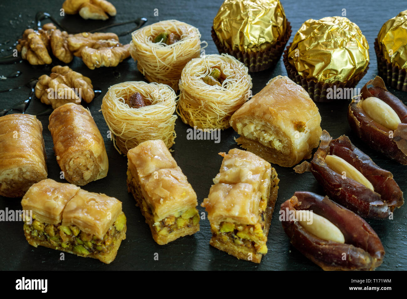 different type of arabian sweets background baklava borma nest ush-el-bul-bul asabi dates and chocolate on black stone background Stock Photo