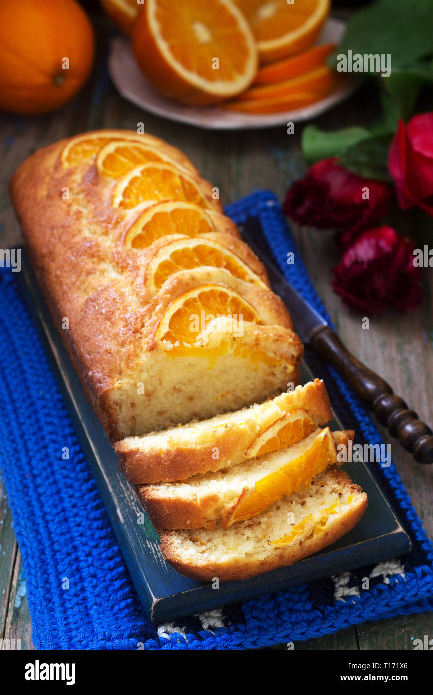 Orange cake, decorated with slices of orange on a background of juicy oranges and a bouquet of tulips. Rustic style. Stock Photo