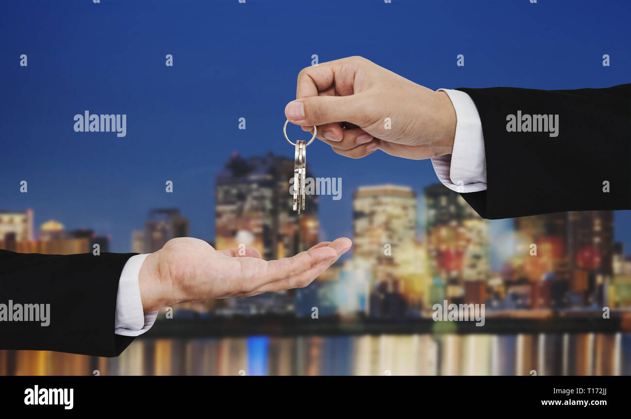 Real estate business, residential rental and investment. Businessman handover keys, with city at night backgrounds Stock Photo