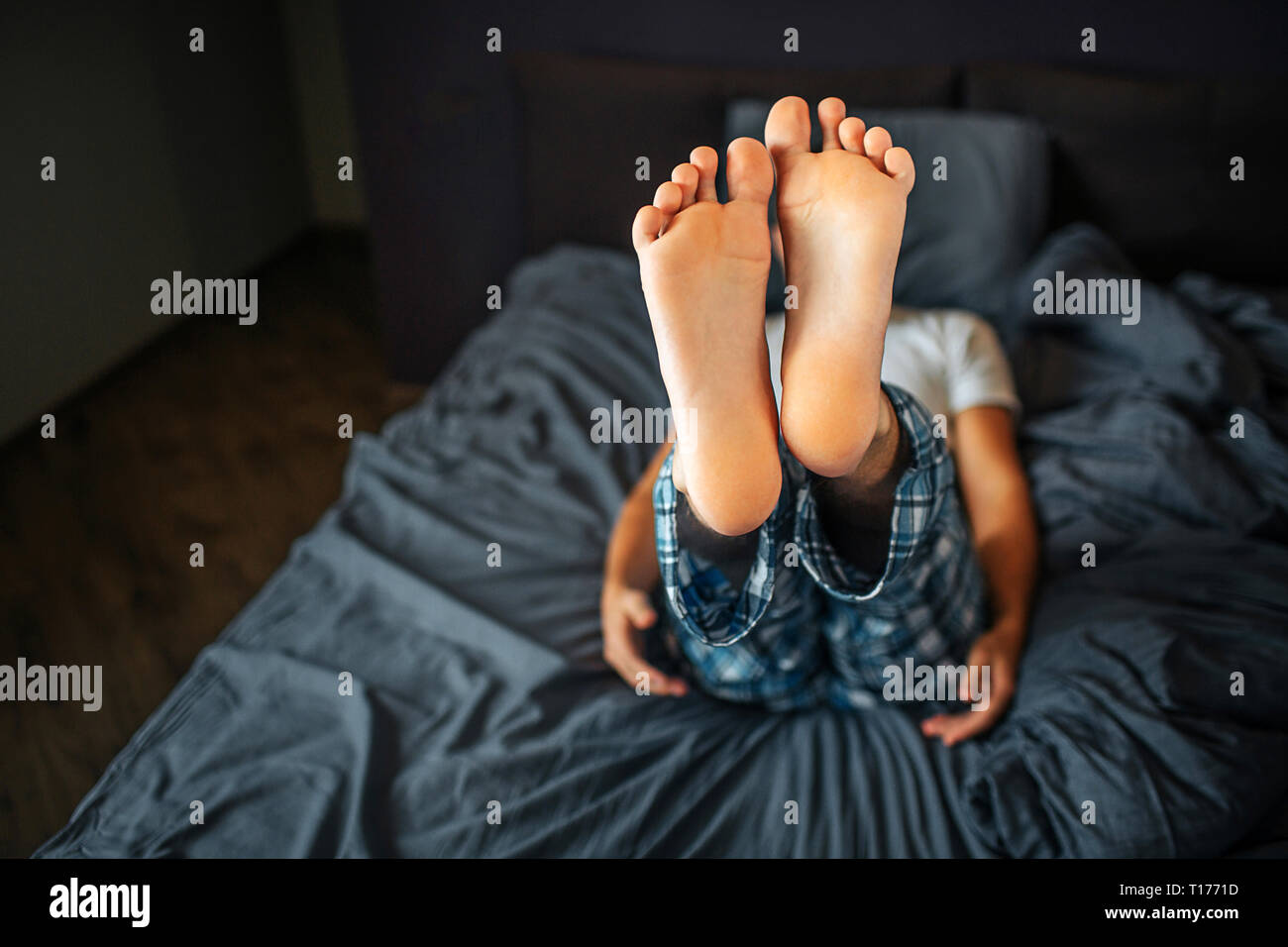Picture of man lying on bed and showing both feet on camera. Skin are healthy and clean. Man is in bedoom. He wears pajamas. Stock Photo