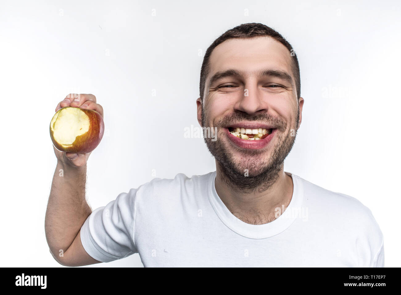 Happy and glad young guy is happy he doesn't have problems with teeth and gums. They are clean, healthy and good. Also he has bitten a piece of apple Stock Photo