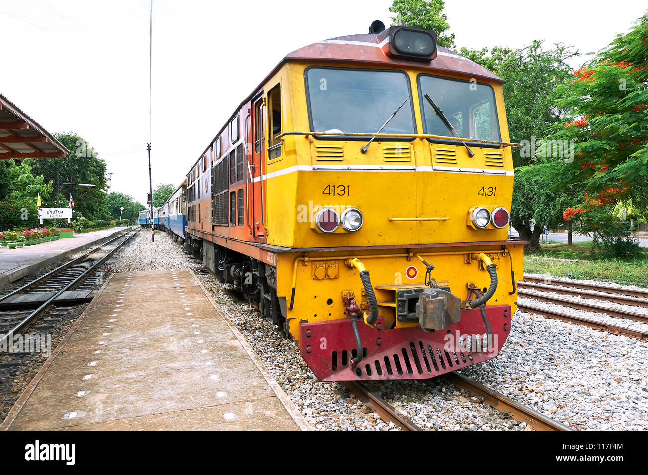 Ban Pong, Thailand - June 20, 2011: Long colorful diesel train entering the train station. There are no passengers on the platform. Stock Photo