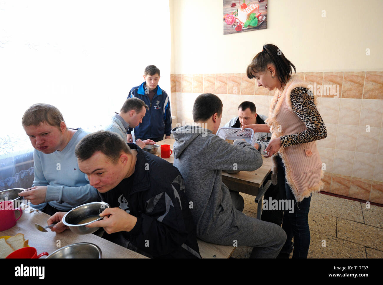 At the canteen of the boarding school for disabled children. Down syndrome boys sitting at tables, waitress serving . February12, 2019. Kiev,Ukraine Stock Photo