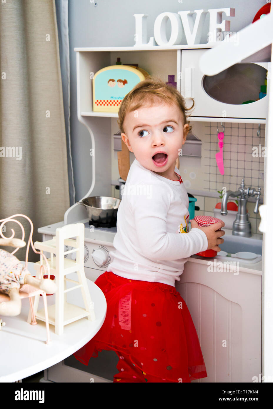 young Caucasian girl playing with toy kitchen at home. Stock Photo