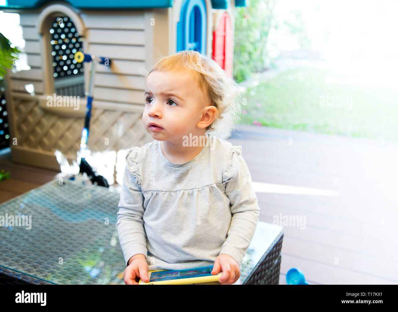 young girl 3yrs old looking to right, with a bored,facial expression  sitting in garden. Stock Photo