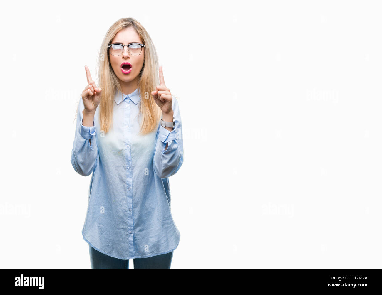 Young beautiful blonde business woman wearing glasses over isolated background amazed and surprised looking up and pointing with fingers and raised ar Stock Photo