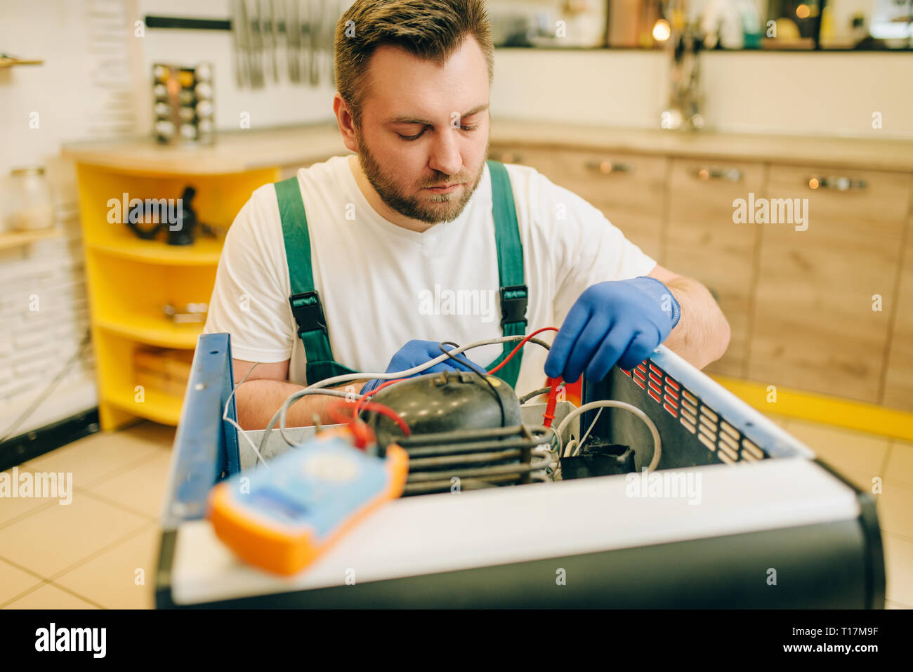 Worker in uniform testing refrigerator at home Stock Photo