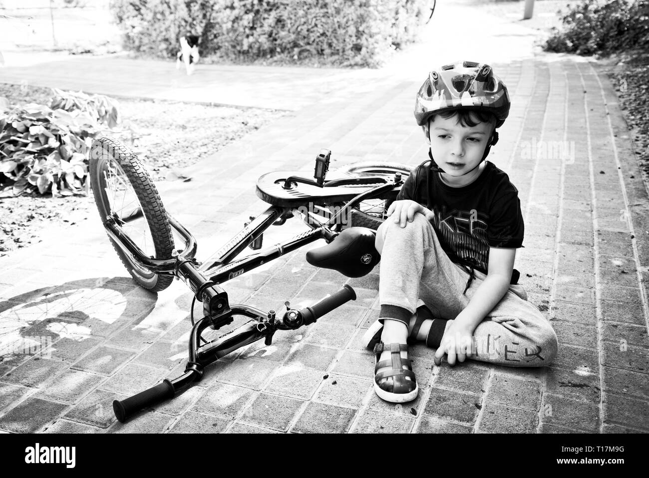 boy holding his knee after falling off bike on paved pathway.determined to get back on after the  accident, Stock Photo
