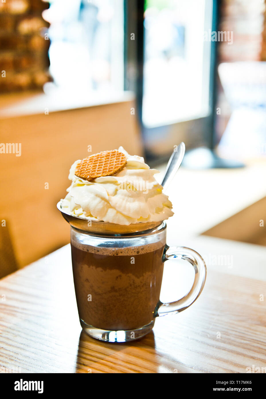 One glass of hot chocolate topped with fresh cream and round biscuit against a light window background,indoors. Stock Photo