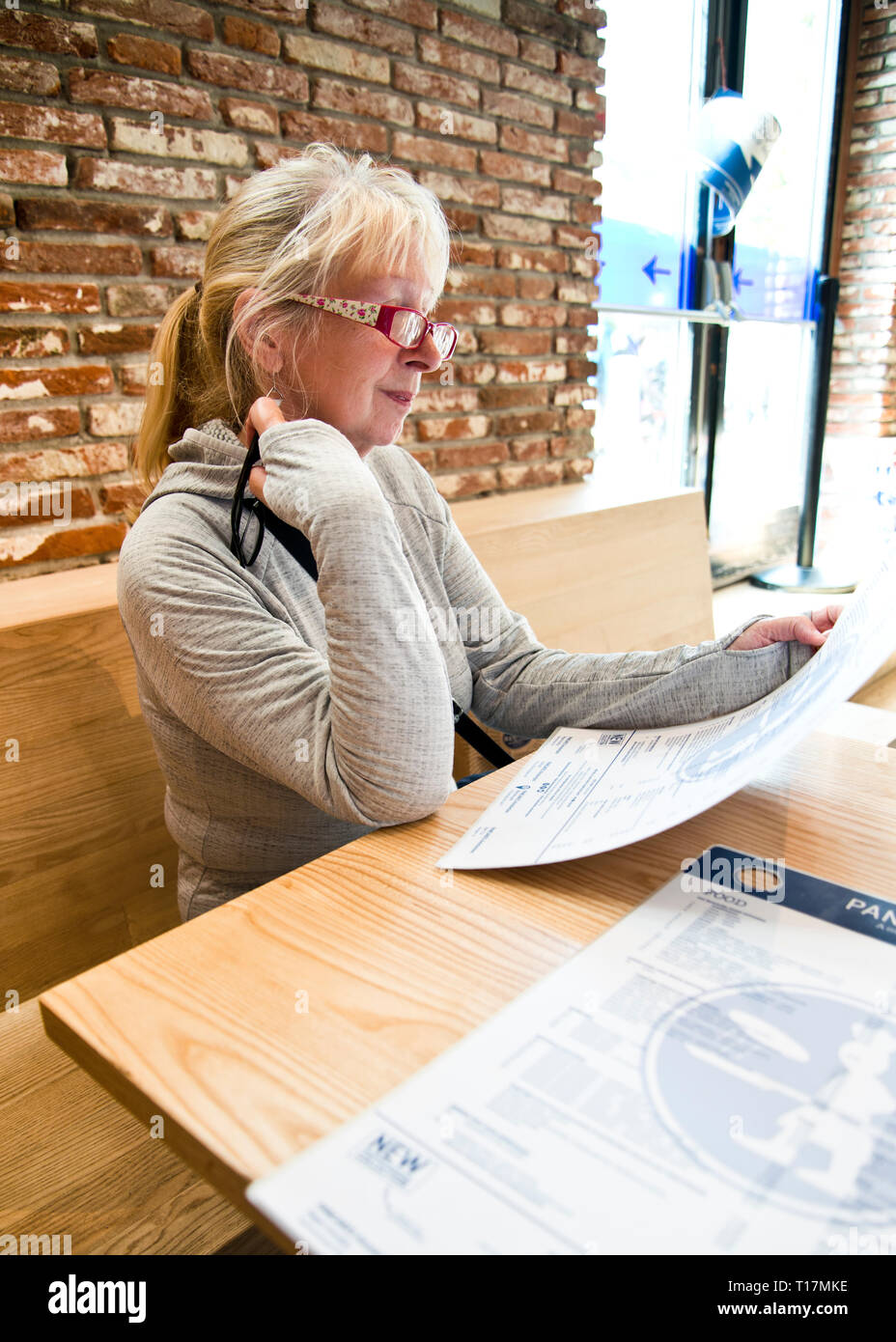 Middle aged woman sitting alone in casual dinning cafe, looking down at the menu in modern styled cafe with basic interior furnishings Stock Photo