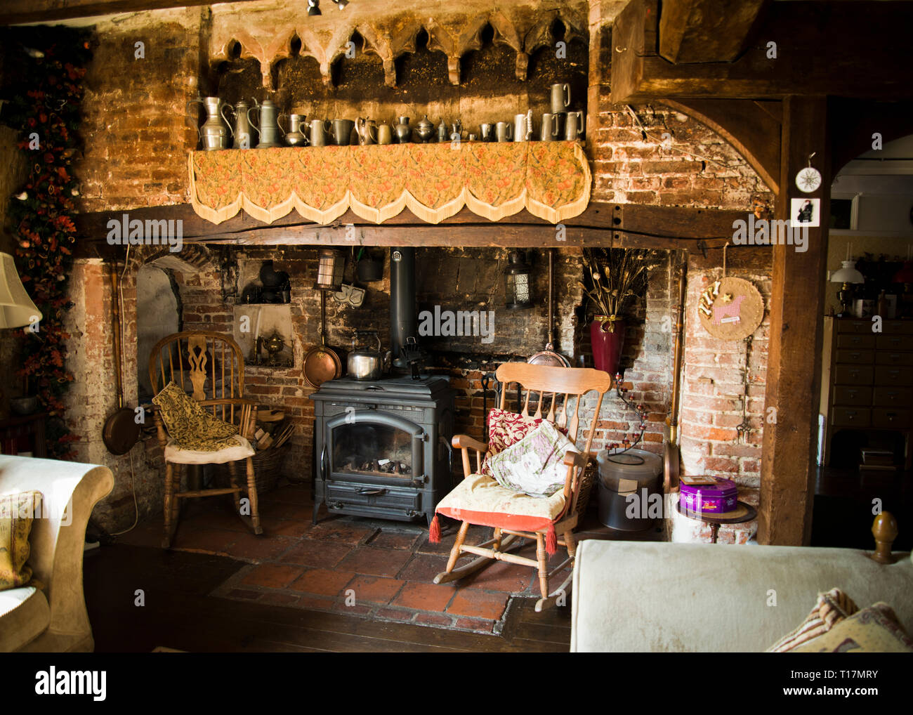 Old fireplace in the drawing room of an old country village home surrounded with decorative antique furniture and interesting objects hanging on walls Stock Photo