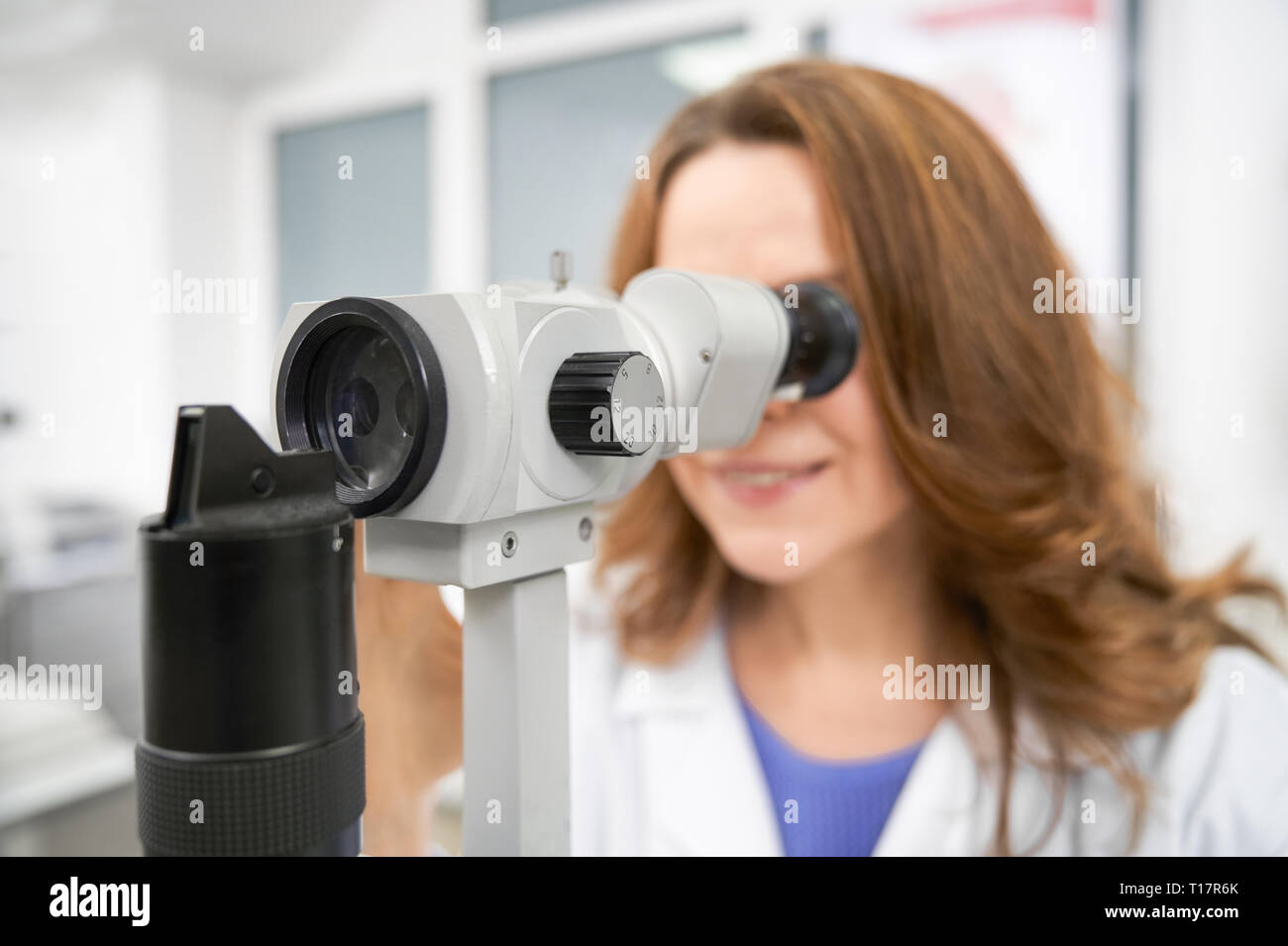 Close up of ophthalmologist looking in slit lamp. Beautiful woman working in medical clinic and examining eyesight using special equipment, eye test machine. Concept of health care. Stock Photo