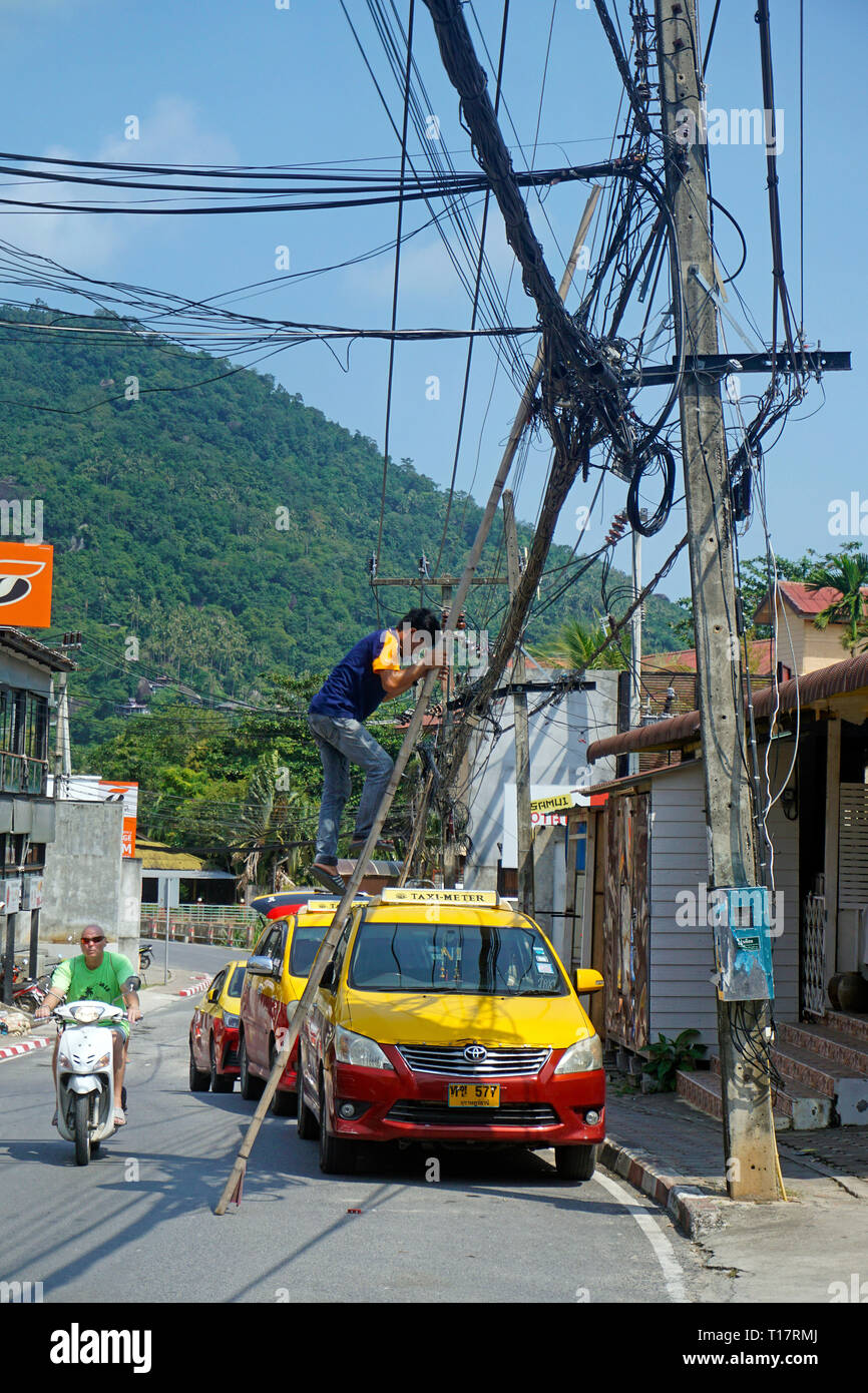 Electrical worker climbs up a ledder to repair power supply, downtown, Lamai Beach, Koh Samui, Surat Thani, Gulf of Thailand, Thailand Stock Photo