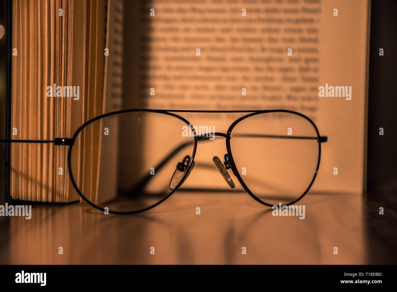 Close up of glasses laying on a table in front of a open book Stock Photo