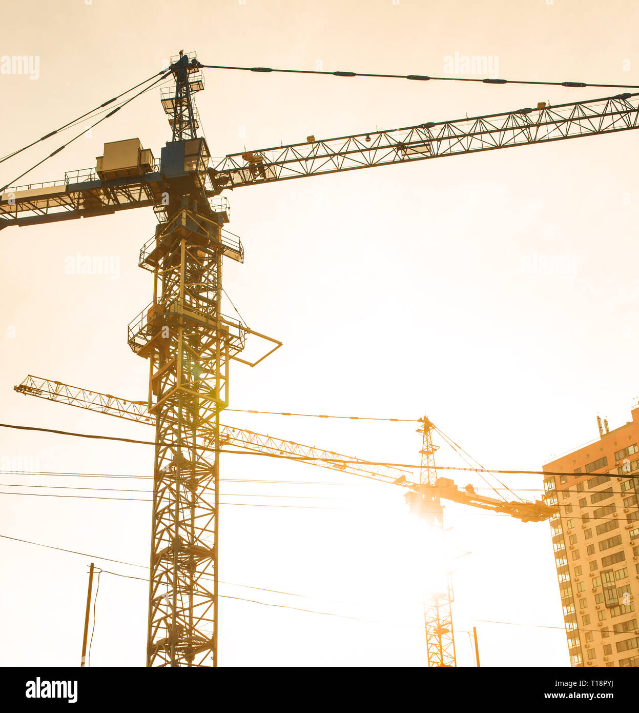 Building site with high-rise block under construction in an urban environment dominated by a large industrial crane silhouetted against sunset sky Stock Photo