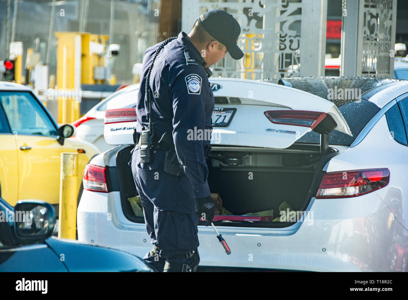 A border patrol officer going car to car at the San Ysidro border crossing with a mirror, to peek underneath vehicles. Stock Photo