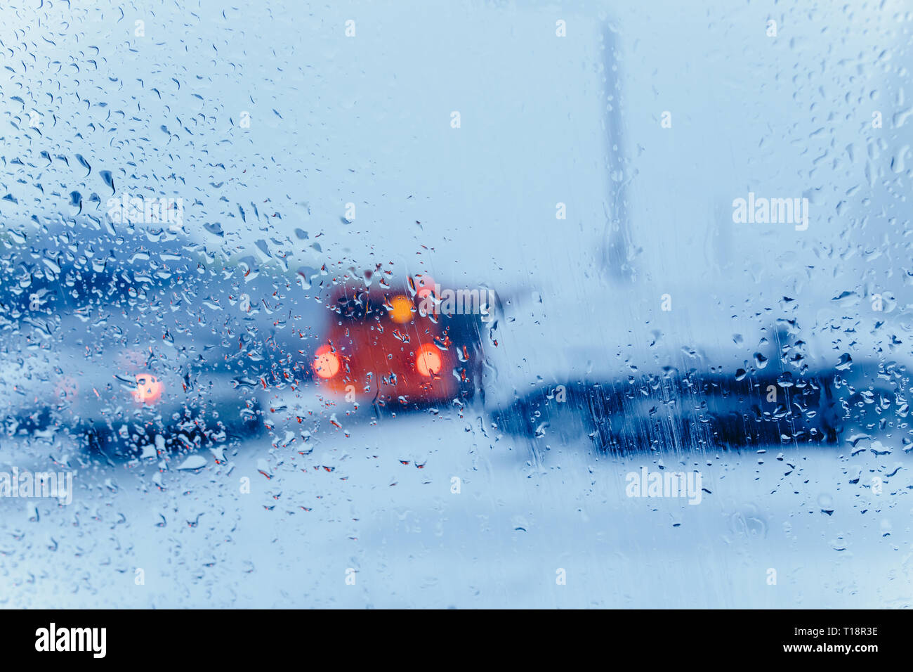 Traffic abstract in winter. Traffic seen from inside a car. Water drops on windshield and car tail lights in bokeh Stock Photo