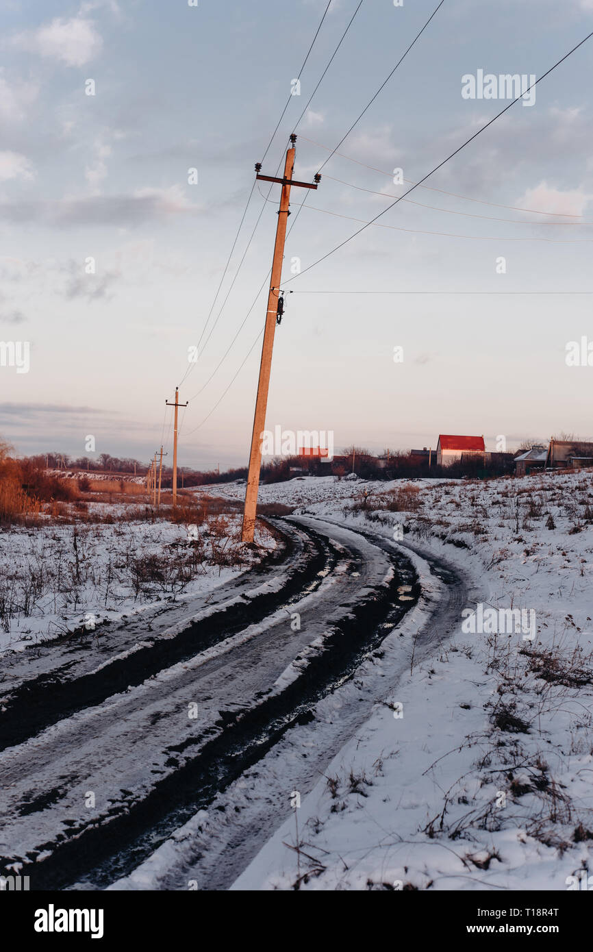 Country dirt road with muddy puddles and melting snow in early spring at sunset Stock Photo