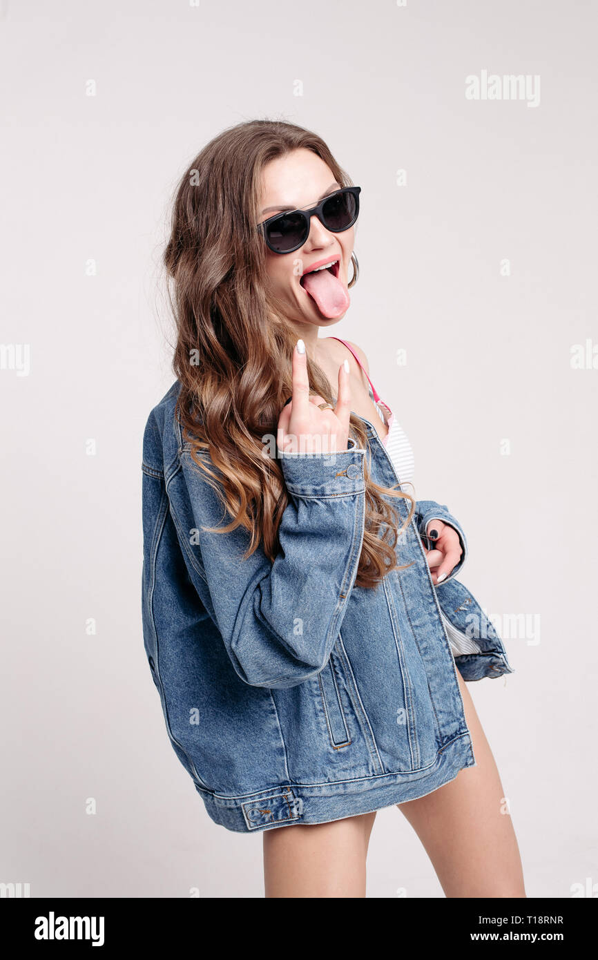 Funky girl in stylish sunglasses and denim jacket shows rock sign with ...