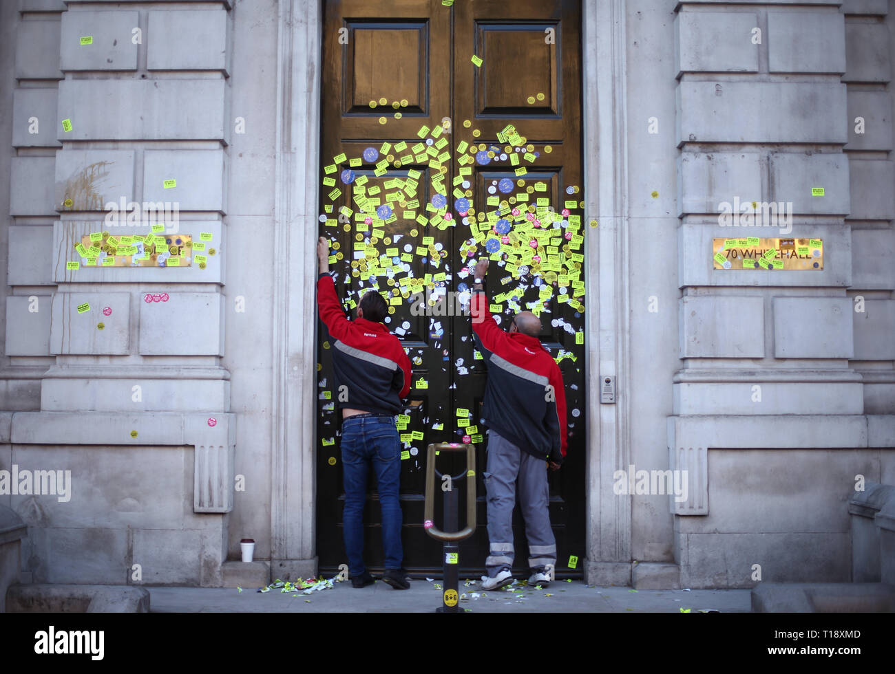 Workers peeling off stickers left on the Cabinet Office door on Whitehall, London, left by anti-Brexit campaigners after they took part in the People's Vote March. Stock Photo