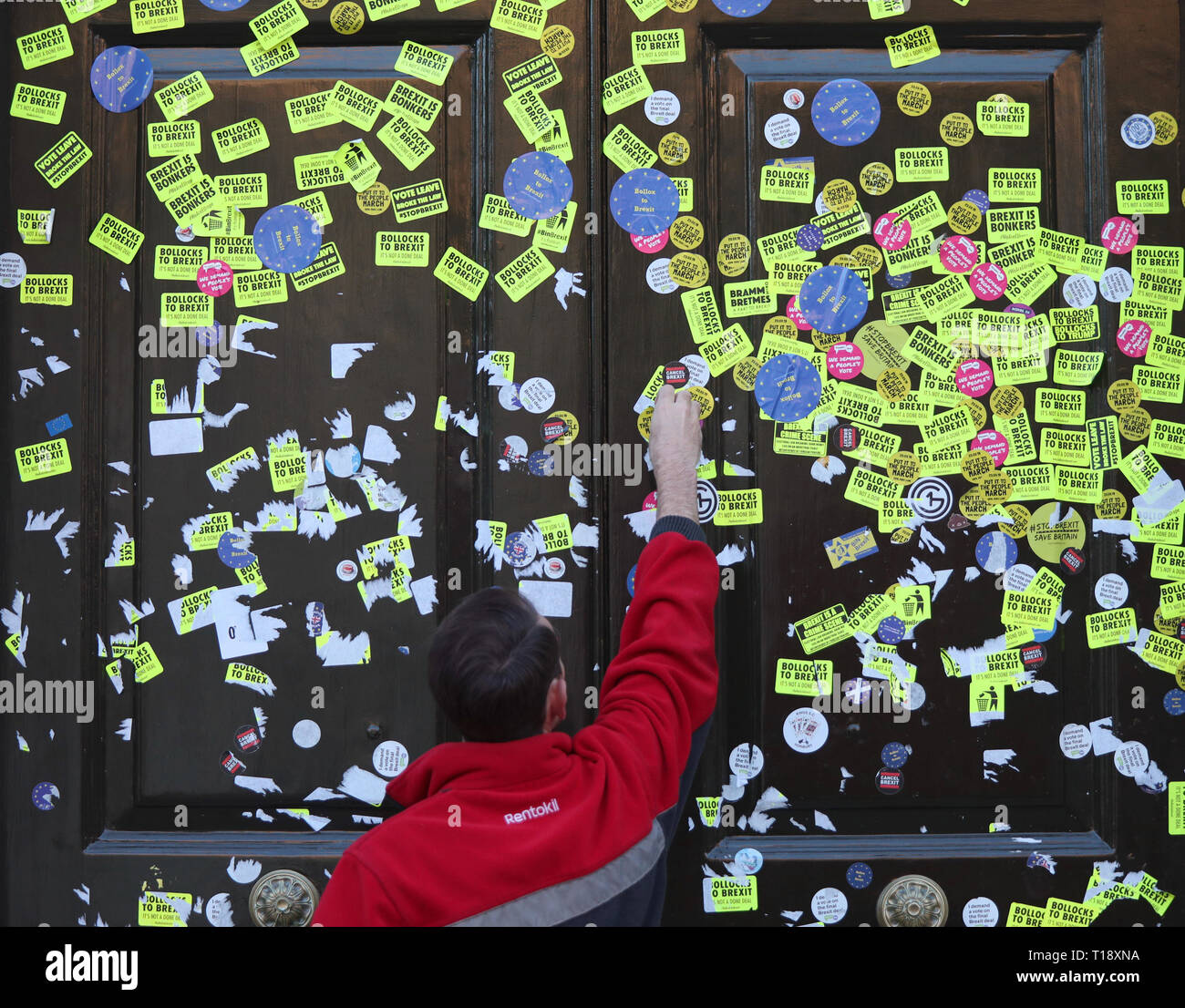 Workers peeling off stickers left on the Cabinet Office door on Whitehall, London, left by anti-Brexit campaigners after they took part in the People's Vote March. Stock Photo