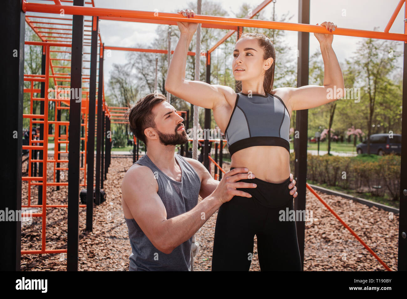 Two attractive people are standing outside. Girl is pulling herself up
