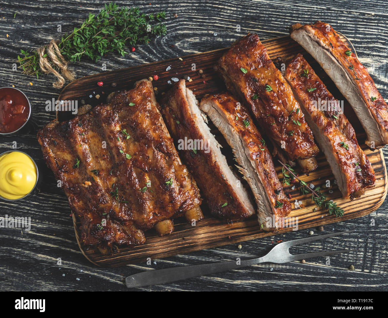 cutting grilled pork ribs with sauce on a board, spices, wooden background Stock Photo