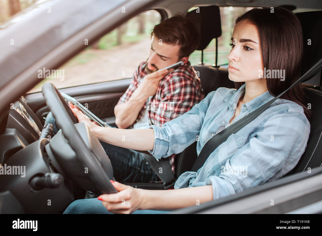 A picture of couple travelling in car. Guy is talking on the phone while girl is driving and paying attention to the road. She looks serious Stock Photo