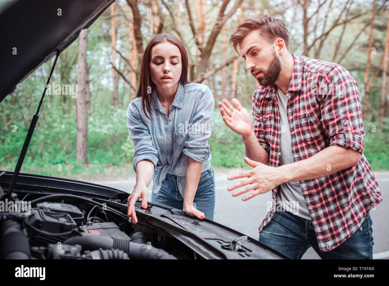 A picture of couple trying to fix the engine of car. It got broken. Girl is