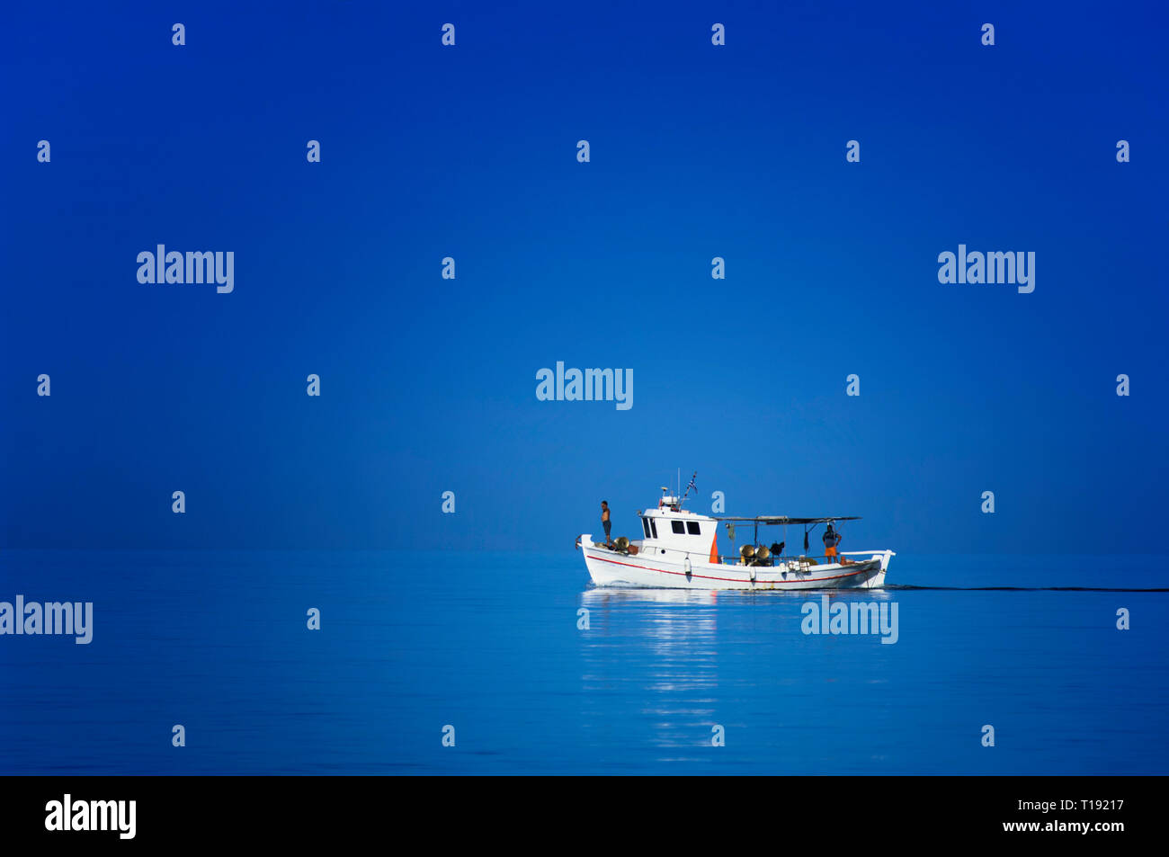 A traditional Greek fishing boat in the Aegean Sea isolated under a cloudless sky Stock Photo