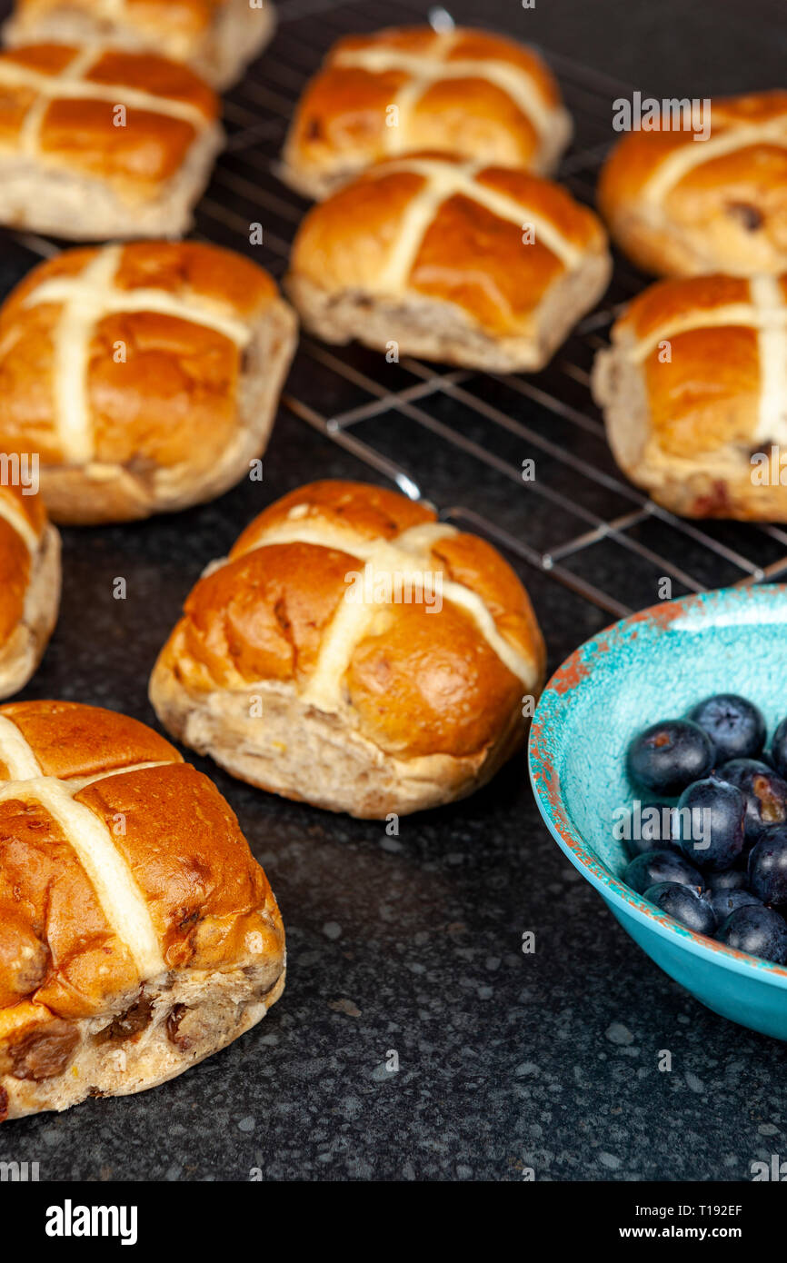 Freshly baked hotcross buns on a granite work surface with a bowl of blueberries Stock Photo