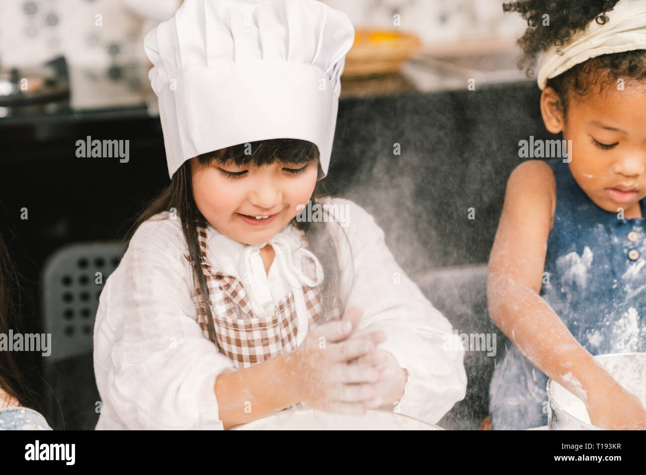 Cute mixed race and African American kid girls baking or cooking together in home kitchen. Education activity, youth culture, or smart young children  Stock Photo