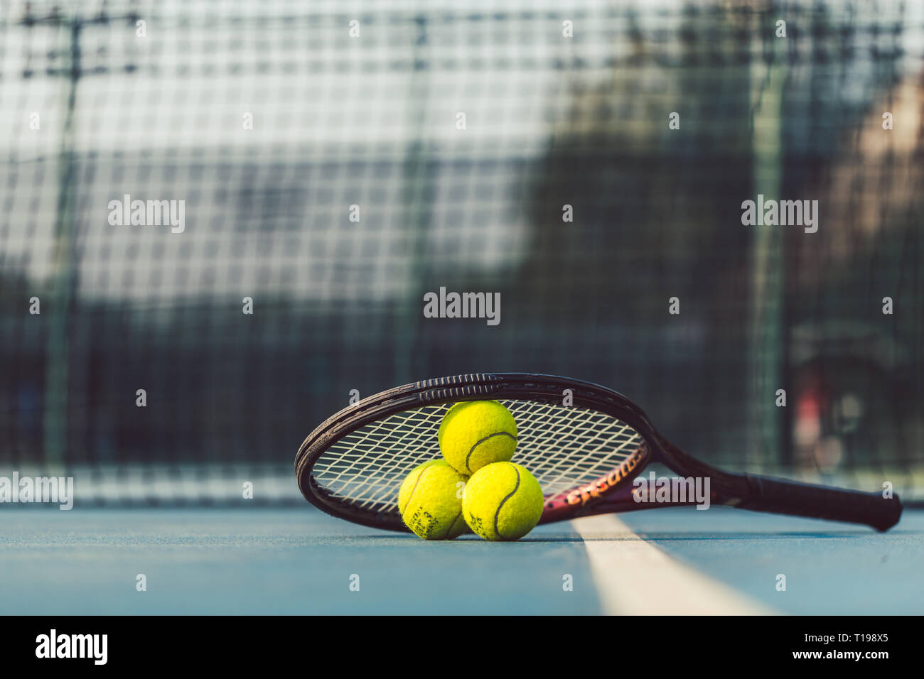 Three tennis balls on a professional racket on acrylic blue surface Stock Photo