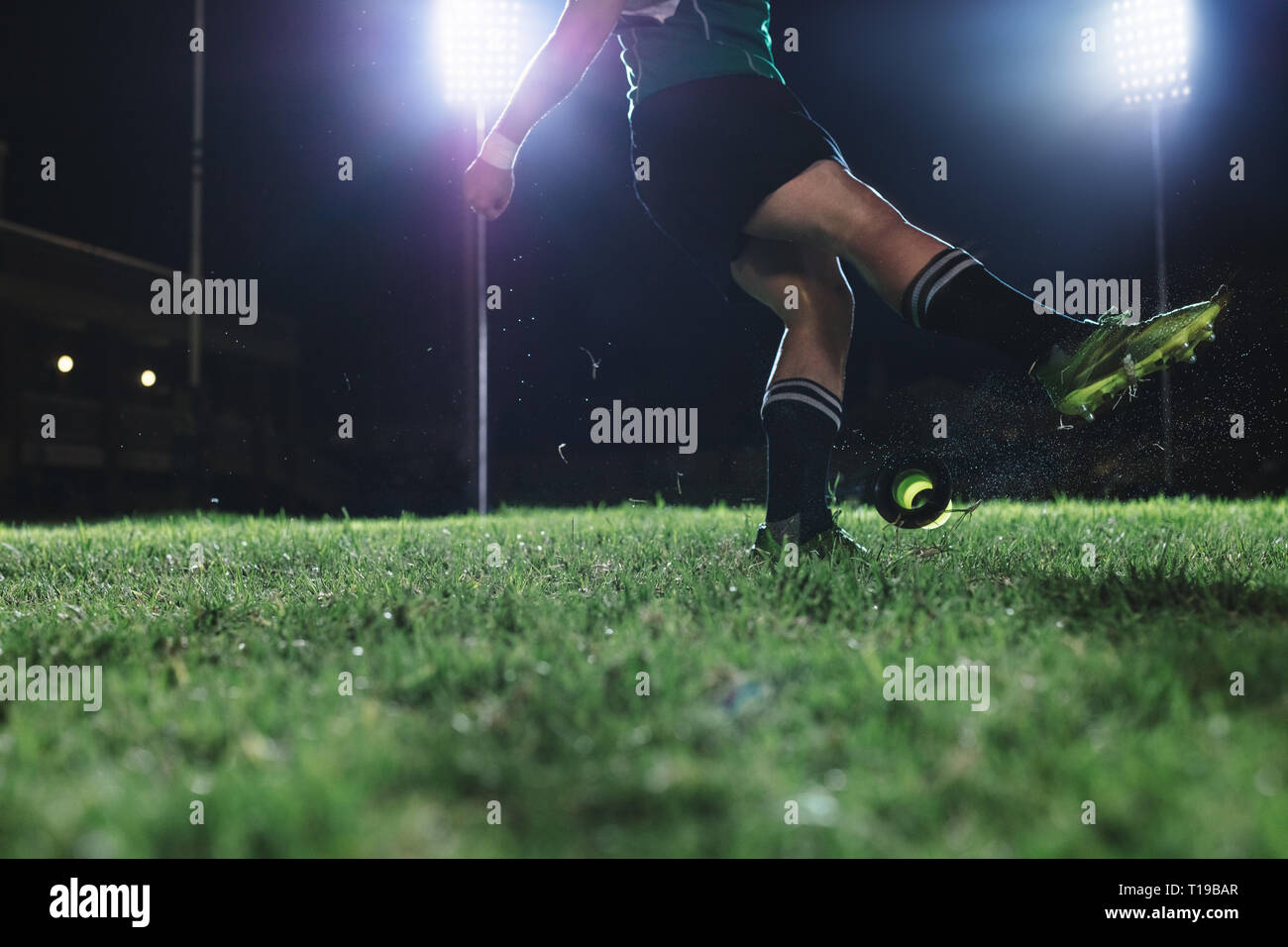 rugby player kicking the ball from a tee for penalty shot. Legs of professional rugby player kicking the ball under lights at rugby stadium at night. Stock Photo