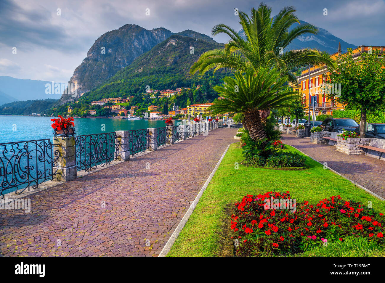 Summer holiday location, spectacular promenade with colorful flowers in public park and palm trees on the shore, Lake Como, Menaggio, Lombardy region, Stock Photo