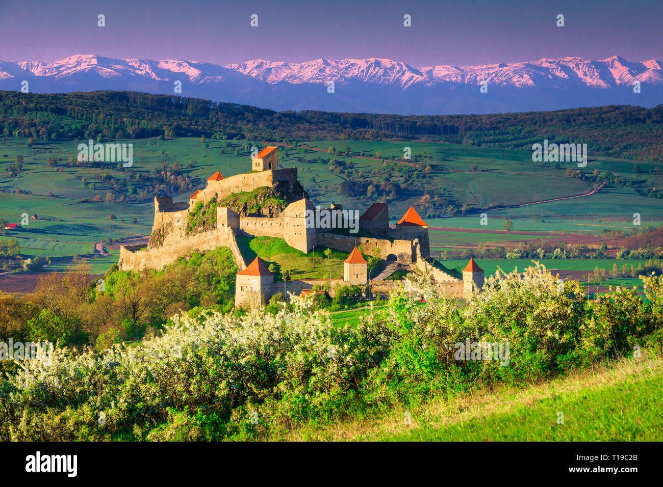 Fantastic tourist attraction and travel location. Well-known Rupea fortress and snowy mountains in background at sunrise, Brasov, Transylvania, Romani Stock Photo